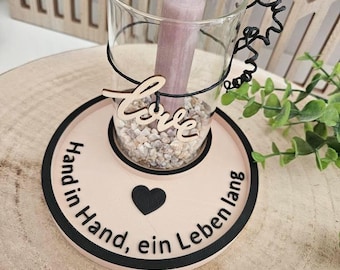 May include: A wooden candle holder with a glass votive and a pink candle. The holder has the words "Hand in Hand, ein Leben lang" and a heart on it. The word "Love" is written on a separate wooden piece.