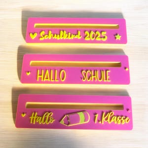 Könnte beinhalten: Drei rosa rechteckige Schilder mit gelber Schrift. Das obere Schild lautet "Schulkind 2025" mit Herz und Stern. Das mittlere Schild sagt "Hallo Schule". Das untere Schild sagt "Hallo 1. Klasse" mit einer Bleistiftgrafik.
