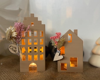 May include: Two decorative wooden house-shaped candle holders. The larger one has multiple windows, while the smaller one has a single window. Both are adorned with dried flowers and a wooden heart. The larger one has the text "für Dich".