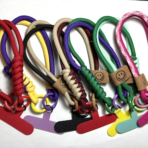 Pode incluir: Uma coleção de oito chaveiros de paracord coloridos com um amuleto de rosto sorridente e um clipe em forma de T. Os chaveiros são feitos com diferentes cores de paracord, incluindo vermelho, amarelo, roxo, verde e rosa.
