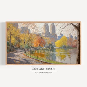 Op de afbeelding: Een ingelijste kunstdruk van een parkscène in de herfst. Het schilderij toont een meer, bomen met gele en oranje bladeren, een pad en gebouwen op de achtergrond. De tekst "NINI ART BRUSH" en "HERITAGE PRINTS ARTISTRY" staat onderaan.