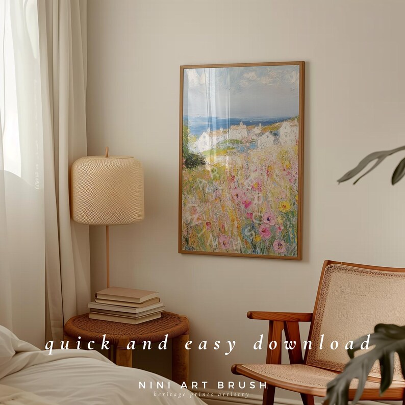 Op de afbeelding: Een ingelijst schilderij van een kustlandschap met witte huizen en een veld vol bloemen in tinten roze, geel en wit. Het schilderij is in een licht houten lijst en hangt aan een witte muur.