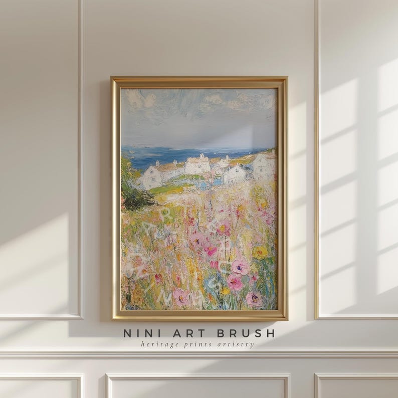 Op de afbeelding: Een schilderij van een kustdorp met witte huizen en een veld met roze en gele bloemen op de voorgrond. De lucht is blauw met witte wolken en de zee is in de verte zichtbaar. Het schilderij is ingelijst in goud.