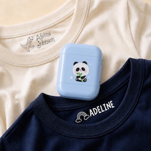 May include: A cream t-shirt with a dinosaur graphic and the text Adeline Johnson, a navy blue t-shirt with a rainbow graphic and the text ADELINE, and a light blue earbud case featuring a panda graphic holding a green bamboo stalk.