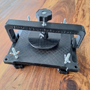 以下が含まれることがあります： ノブとネジが付いた黒い3Dプリントの卓球ボールプレス。プレスには「I &hearts; Table Tennis」という文字が印刷されています。