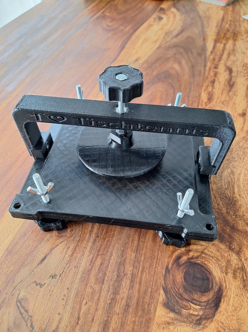 以下が含まれることがあります： ノブとネジが付いた黒い3Dプリントの卓球ボールプレス。プレスには「I &hearts; Table Tennis」という文字が印刷されています。