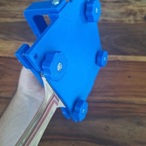 以下が含まれることがあります： 4つの調整可能なノブが付いた青い3Dプリントの卓球ラケットホルダー。ホルダーは卓球ラケットを所定の位置に固定するように設計されています。