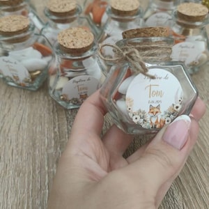 May include: Small glass jars with cork lids filled with white and orange candies. The jars have a fox and floral design with the text "Bapteme de Tom 05.06.2021".