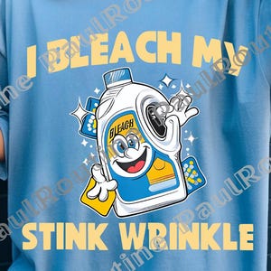 Puede incluir: Camiseta azul claro con el texto amarillo "I BLEACH MY STINK WRINKLE". La camiseta presenta una imagen de dibujos animados de una botella de lejía sonriente, sosteniendo una esponja y un diamante.