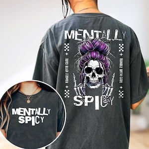 May include: Dark grey t-shirt with the text "MENTALLY SPICY" and a skull graphic with purple hair. The back of the shirt features the same graphic and the words "HANDLE WITH CARE". The shirt is a casual style.