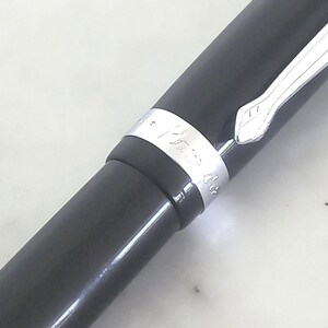 K&ouml;nnte beinhalten: Nahaufnahme eines schwarzen F&uuml;llfederhalters mit silbernem Band. Der Stift hat eine glatte, gl&auml;nzende Oberfl&auml;che und einen silbernen Clip. Das Band hat gravierten Text. Der Stift wird wahrscheinlich zum Schreiben und f&uuml;r Kalligraphie verwendet.