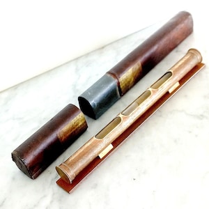 May include: An antique spirit level with a wooden body and brass detailing, shown with its leather case. The level has several viewing windows and sits on a brown base. The case is brown with a metal end.