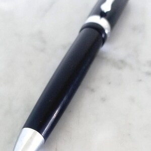 K&ouml;nnte beinhalten: Ein schwarzer Kugelschreiber mit silbernen Akzenten. Der Stift hat eine silberne Spitze und einen silbernen Clip. Er liegt auf einer wei&szlig;en Marmoroberfl&auml;che. Der Stift ist ein Schreibger&auml;t.
