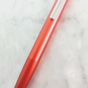 May include: A vibrant red pen with a silver clip. The pen has a sleek, streamlined design and a glossy finish. The pen is a writing instrument.