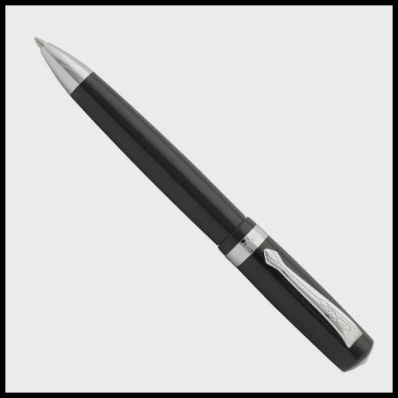 K&ouml;nnte beinhalten: Ein schwarzer Kugelschreiber mit silberner Spitze und Clip. Der Stift hat eine glatte, gl&auml;nzende Oberfl&auml;che und ein silbernes Band in der Mitte. Der Clip ist rechteckig mit einem dekorativen Design. Der Stift ist vor einem hellgrauen Hintergrund abgebildet.