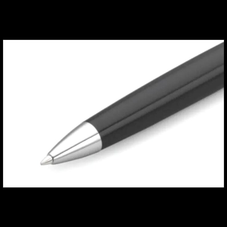 K&ouml;nnte beinhalten: Nahaufnahme eines schwarzen Kugelschreibers mit silberner Spitze. Der Stift hat eine glatte, gl&auml;nzende Oberfl&auml;che und ein schlichtes, elegantes Design. Der Stift ist leicht angewinkelt, wodurch seine stromlinienf&ouml;rmige Form und die Metallspitze zur Geltung kommen.