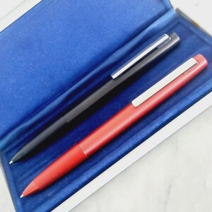 May include: Two pens, one black and one red, are displayed inside a blue velvet-lined box. Each pen has a silver clip. The red pen is in the foreground, and the black pen is behind it.