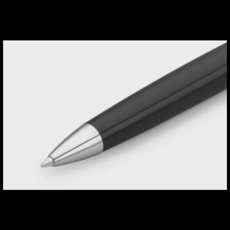K&ouml;nnte beinhalten: Nahaufnahme eines schwarzen Stifts mit silberner Spitze. Der Stift hat eine elegante, gl&auml;nzende Oberfl&auml;che und eine konische Silberkappe. Der Stift ist leicht angewinkelt und zeigt sein Design vor einem wei&szlig;en Hintergrund.