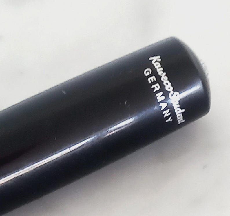 K&ouml;nnte beinhalten: Nahaufnahme eines schwarzen Stifts mit dem wei&szlig;en Aufdruck "Kaweco Student GERMANY". Der Stift hat eine glatte, gl&auml;nzende Oberfl&auml;che und eine abgerundete Spitze. Der Stift ist leicht angewinkelt, wodurch die Schrift auf der Seite zu sehen ist.
