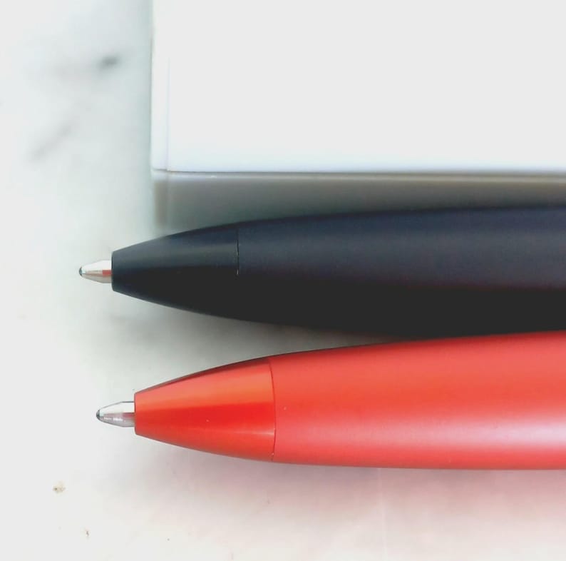 May include: Close-up of two pens. One pen is black, and the other is red. Both pens have a silver tip and a sleek, modern design. The pens are positioned horizontally against a white background.