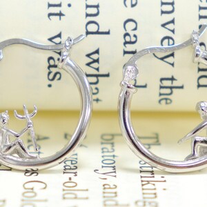 May include: A pair of silver hoop earrings with a small angel and a small devil charm hanging from each hoop.