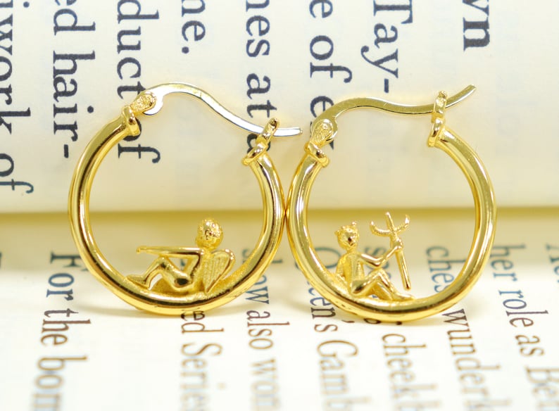 May include: A pair of gold hoop earrings with a small angel and a small figure holding a trident hanging from each hoop.