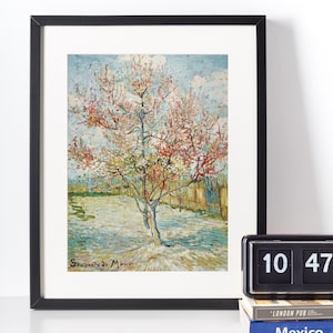 May include: A framed art print depicting a blossoming tree with pink and white flowers, set against a blue sky. The artwork, in a black frame, has a detailed painting style with visible brushstrokes, evoking spring. The print is displayed on a white wall.