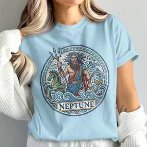 Light blue t-shirt with circular mosaic art of Neptune holding a trident, with horses and dolphins.
