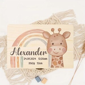 以下が含まれることがあります： 虹と可愛いキリンのイラストが描かれた木製看板。看板には「Alexander」という名前、日付「24.09.2024」、時間「12:20am」、体重「3562g」、身長「52cm」がパーソナライズされています。