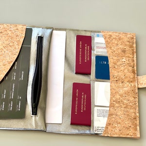 Könnte beinhalten: Eine Reisegeldbörse aus Kork mit einem Reißverschlussfach, zwei Passfächern und mehreren Kartenfächern. Die Geldbörse ist geöffnet und zeigt eine Bordkarte, zwei Pässe und mehrere Karten.