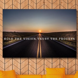 Op de afbeelding: Een motiverend citaat, "Hold the vision, trust the process", wordt weergegeven op een canvasprint met een lange, rechte weg die naar een ondergaande zon leidt.
