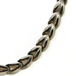 May include: A silver-toned necklace featuring a series of connected, leaf-shaped links. The links have a polished, reflective surface, creating a sleek and modern aesthetic. The necklace is displayed against a white background.