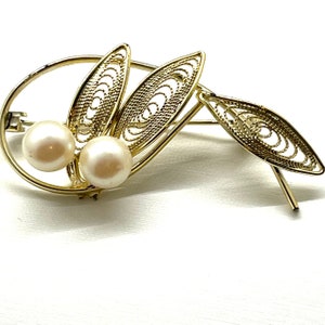 May include: A gold filigree brooch with two white pearls. The brooch is shaped like two leaves.