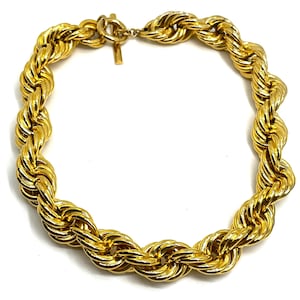 May include: A gold-colored necklace with a rope chain design. The necklace is made of a shiny, metallic material and features a clasp closure. The chain is thick and twisted, creating a bold and eye-catching look. Jewelry.