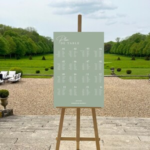 May include: A sage green rectangular wedding seating chart sign displayed on a wooden tripod easel. The sign features the text Plan De Table, sixteen numbered table columns with guest names, the date 20.09.2025, and Domaine De Chantilly.