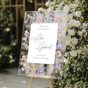 May include: A rectangular clear acrylic wedding welcome sign featuring a central white panel with the text Bienvenue au mariage de Alix et Gabriel 30|08|2026 Château de Chantilly, surrounded by a watercolor floral border of purple, pink, and yellow flowers.