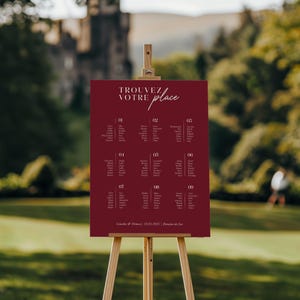 May include: A burgundy wedding seating chart on an easel with the text "TROUVEZ VOTRE place" in white script. The chart lists guest names and table numbers.