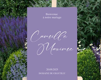 May include: A rectangular purple wedding welcome sign displayed on a light wood easel. The sign features the white text Bienvenue à notre mariage, the names Camille and Maxime in a white script font, and the date 20.09.2025 with Domaine de Chantilly.