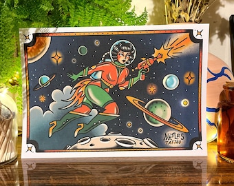 May include: A retro-style illustration of a woman in a spacesuit flying through space. She is holding a ray gun and is surrounded by stars, planets, and a moon. The illustration is in a traditional tattoo style with bold lines and bright colors. The text "Nettles Tattoo" is at the bottom of the image.