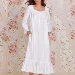 Può includere: Camicia da notte lunga bianca con maniche lunghe, scollatura quadrata e orlo a balze. La camicia da notte ha un'abbottonatura frontale e tasche. Lo sfondo presenta una carta da parati floreale con rose rosa.