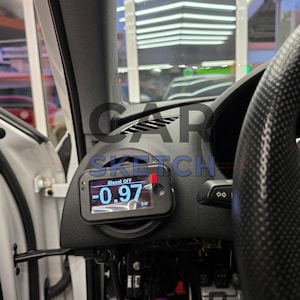 Op de afbeelding: Een close-up van het interieur van een auto met een digitale boostmeter die "iBoost OFF -0.97 bar" weergeeft. De meter is gemonteerd op het dashboard en is omgeven door zwarte bekleding.