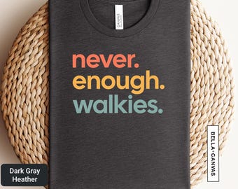 以下が含まれることがあります： オレンジ、黄色、ティール色の「never. enough. walkies.」という文字が入った濃いグレーのヘザーTシャツ。シャツは織り込まれた表面にあります。「Canvas」というブランド名がタグに表示されています。