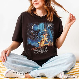 Pu&ograve; includere: T-shirt color cioccolato fondente con grafica di Star Wars. Il design mostra Darth Vader, Luke Skywalker e altri personaggi. Il logo di Star Wars &egrave; bianco.