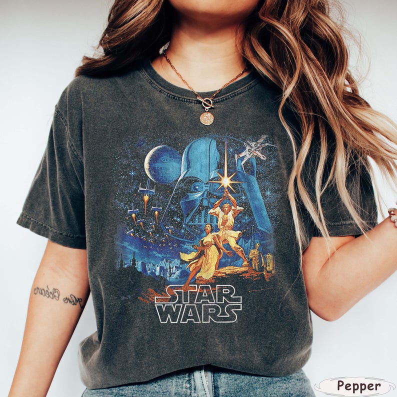 Pu&ograve; includere: T-shirt grigio scuro con grafica di Star Wars. La grafica raffigura Darth Vader, Luke Skywalker e altri personaggi, con la scritta "STAR WARS" a blocchi bianchi.
