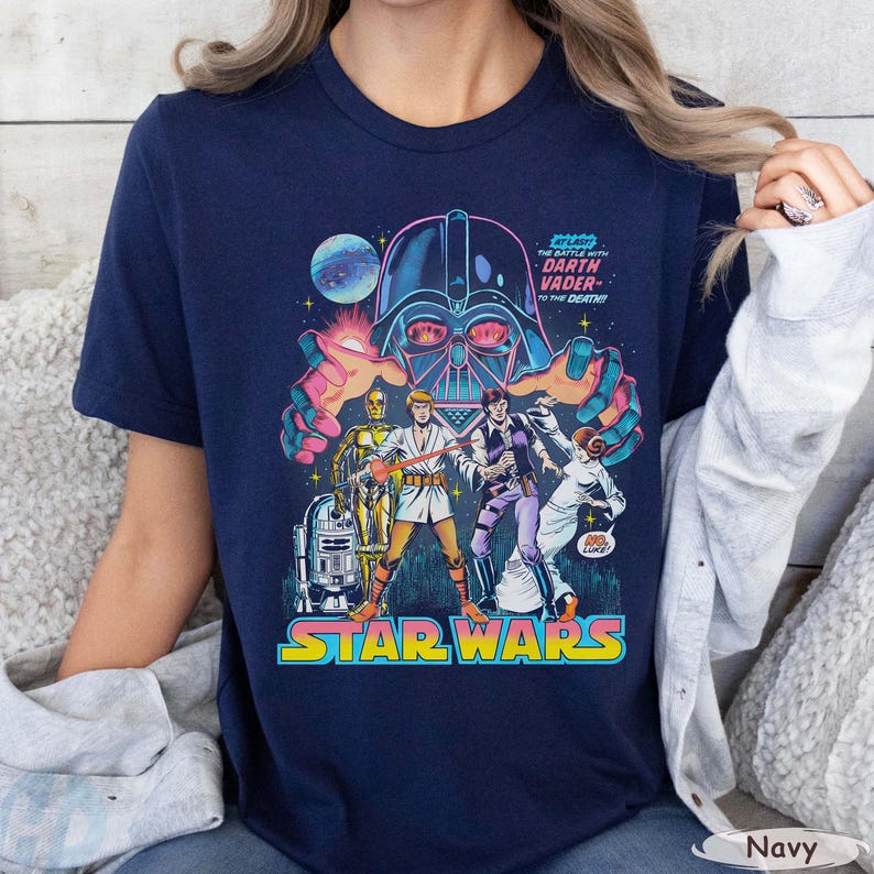 May include: Navy blue Star Wars t-shirt featuring a comic book style graphic. The design includes Darth Vader, C-3PO, R2-D2, and other characters. The text "The Battle with Darth Vader - To the Death!" is also visible.