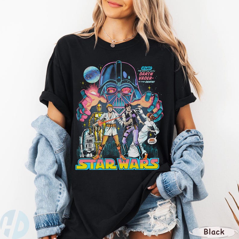 May include: Black Star Wars graphic tee featuring Darth Vader and other characters. The design includes the text "STAR WARS" in a colorful, retro font, and the phrase "THE BATTLE WITH DARTH VADER TO THE DEATH!"