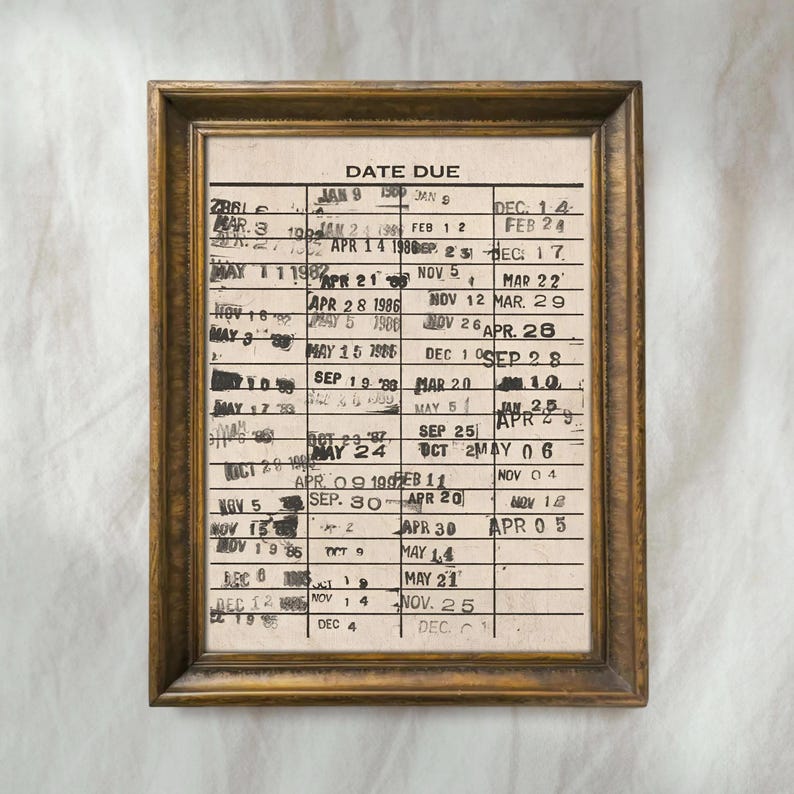 May include: A framed vintage library card with the words "DATE DUE" at the top. The card has multiple entries with dates and stamps, encased in a wooden frame with a gold finish. The overall aesthetic is nostalgic and antique.