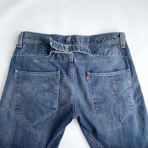 Puede incluir: Vaqueros azules de mezclilla con un diseño único de trabillas y dos bolsillos traseros. Los vaqueros presentan una etiqueta roja en el bolsillo trasero y una forma de bolsillo distintiva. Los vaqueros están hechos de un material de mezclilla duradero.