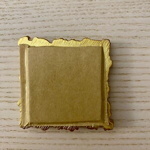 May include: A gold-colored picture frame with a textured, ornate border. The frame is empty and has a brown backing.