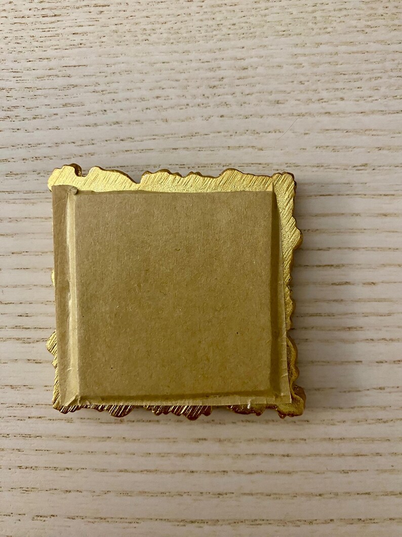 May include: A gold-colored picture frame with a textured, ornate border. The frame is empty and has a brown backing.